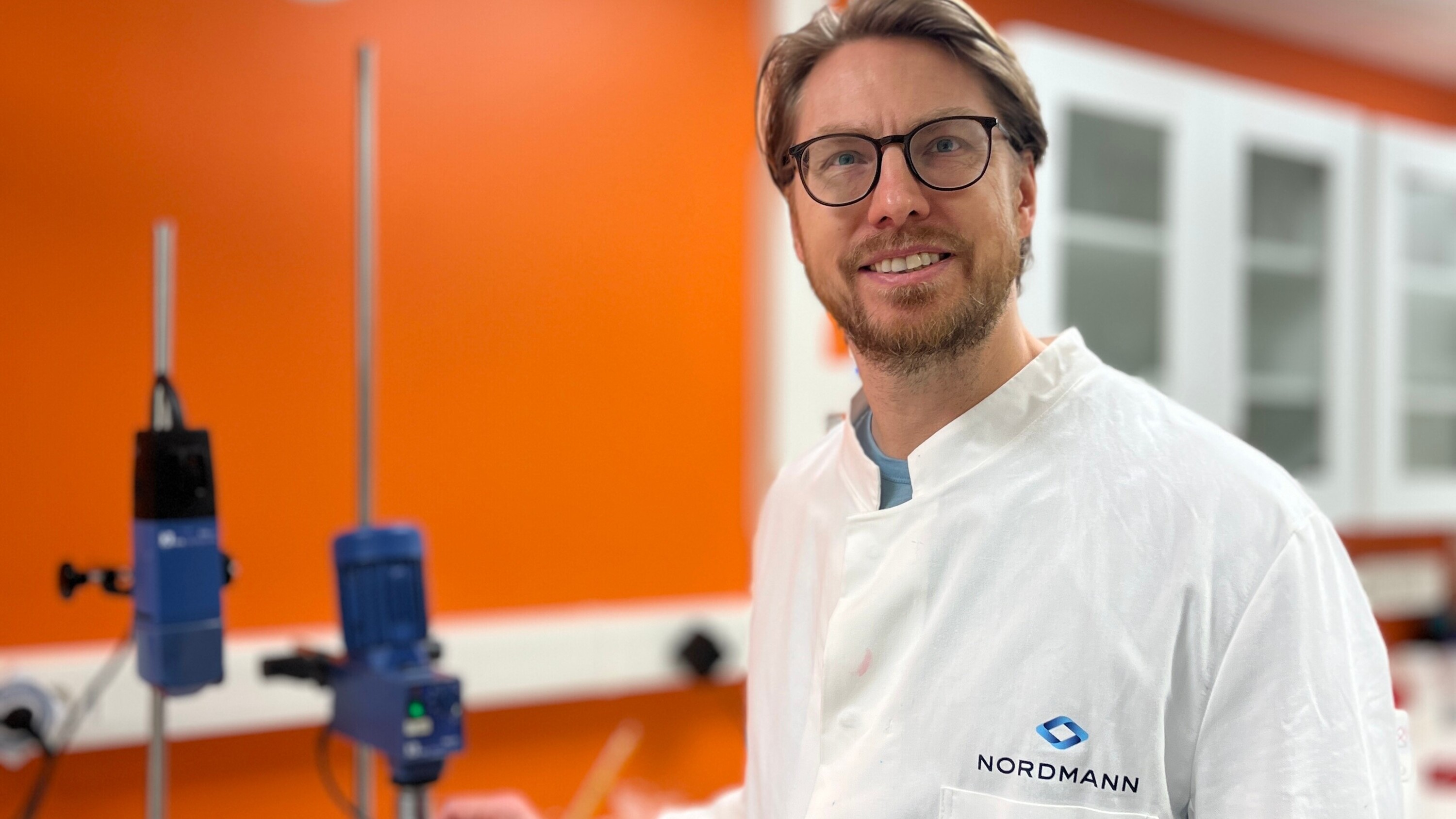 A man, Alf Jarmeus, Senior Application Specialist at Nordmann, standing in a lab with a orange background